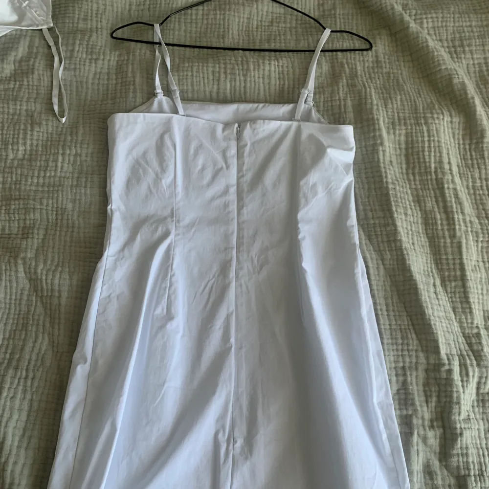 Bandueklänning i vitt med avtagbara band. Har en liten slits i bak. Stretchig men i ett lite ”hårdare” material lite liknande kostym material . Klänningar.