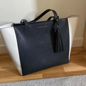 Victoria’s Secret väska (gammal model)  - En rymlig och fin väska, modellen är dock gammal och köpt i Victoria’s secret affären i Göteborg. Lite sliten, men annars väldigt bra skick. Färgen är svart och vit, den har inga fickor inuti väskan men rummet mycket. Nytt pris 1249kr