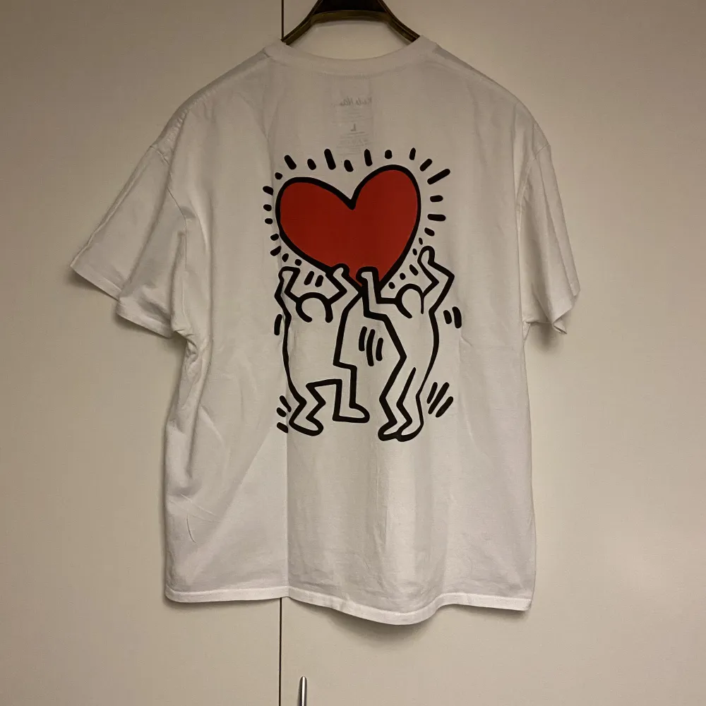 Keith Haring tisha i dunder skick köpt på Urban Outfitters. Hans ikoniska konst på ryggen samt en liten logga där fram av samma motiv. . T-shirts.