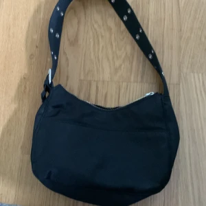 Svart axelväska - En svart axelväska med hål på banden som är köpt från H&M för 299kr men säljer billigt då jag inte använder den längre. Väskan är i bra skick och får plats med mycket i.