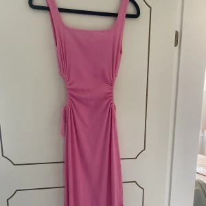 Sommarklänning - Jättefin skrik-rosa ribbad klänning med cut-out detaljer och slits. Materialet är strechigt och hålen går att anpassa storlek på. Se hur klänningen sitter på bild 2&3💞  Köpare står för frakt Skriv vid fler bilder eller intresse🤍