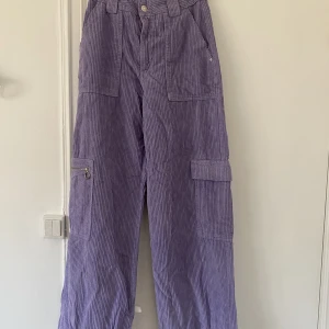 Lila Manchester Byxpr - Lila baggy byxor i manchester. Hög midja och långa ben. Fina detaljer på fickor.  Helt oanvända.