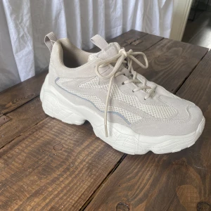 Sneakers 37 - Sneakers köpta från NA-KD. Beige/gråa skor med litet reflexband på sidan. Använda fåtal gånger men ser helt nya ut, finns inga fläckar eller smuts på skorna. Storlek 37 🤎🤍🤎