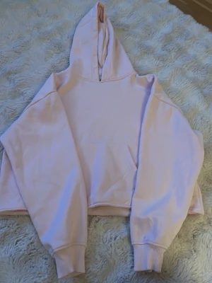 Ljusrosa hoodie med magficka - En oversized ljusrosa hoodie med stor huva och magficka. Tröjan har långa ärmar med breda muddar och är tillverkad i mjukt bomullstyg. Perfekt för en avslappnad och trendig look.