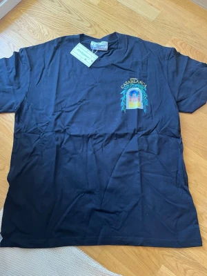 Svart Casablanca t-shirt med tryck - Svart t-shirt från Casablanca med färgglatt tryck av ett fönster och byggnad på bröstet och ryggen. T-shirten har korta ärmar, rund hals och är gjord i mjuk bomull. Perfekt för dig som gillar unika prints och streetwear vibes.
