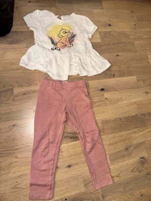 Disney Nala set med topp och leggings - Sött set med vit volangtopp med Nala-tryck från Lejonkungen och rosa leggings. Toppen har kort ärm och volang nertill, tryckt motiv framtill. Leggingsen är enfärgade och mjuka. Perfekt för dig som gillar Disney och vill ha en bekväm outfit.Disney Nala set med topp och leggings