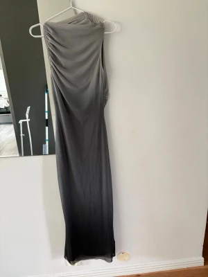 Grå långklänning oneshoulder - Snygg grå långklänning med oneshoulder-design och draperad detalj vid axeln. Klänningen har en smal passform och är tillverkad i ett mjukt, stretchigt material som ger en elegant siluett. Perfekt för dig som vill sticka ut med en stilren look.