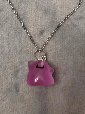 Självlysande Ditto halsband Pokémon smycke  - Så gulligt halsband med en berlock av Ditto!Berlocken är ca 1,5 x 1,5 cm och trädd på en kedja i silverimitation, justerbar 40-45 cm. Betlocken är också självlysande och lyser i mörkret.