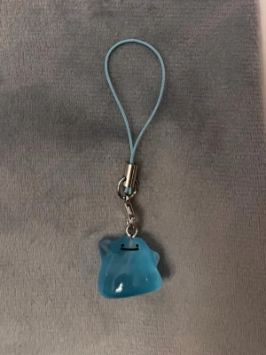 Ditto Mobilsmycke Pokemon hänge Ditto Nyckelring Pokemon Shiny Ditto - Jättegulligt hänge med en blå shiny Ditto! Den är dessutom självlysande och lyser i mörkret.   Ditto-berlocken är ca 1,5 x 1,5 centimeter. Öglan är ca 5 cm lång.  Jättefin att sätta på din mobil, väskan, ditt 3DS, Switch eller i nycklarna exempelvis! 