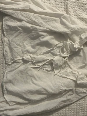 Vit blus med knytning från 157 - Säljer en vit blus från 157 i storlek XS. Blusen har långa ärmar och snygg knytning framtill vid halsen. Tillverkad i ett tunt, luftigt tyg som ger en avslappnad och trendig look. Perfekt att styla med jeans eller kjol för en cool vibe.