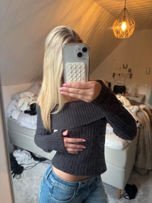 Mörkgrå off shoulder stickad tröja - Säljer en mörkgrå ribbstickad off shoulder-tröja från KappAhl. Tröjan har långa ärmar och en bred krage som sitter snyggt över axlarna. Perfekt för dig som gillar en trendig och bekväm stil till hösten eller vintern.