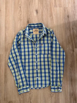 Hollister skjorta ~ Vintage  - Säljer denna skjorta från Hollister. Storlek M. Passar perfekt för dig som är mellan 175-180! Hör av er vid frågor eller minsta fundering 🙌  Märke: Hollister  Storlek: M  Färg: Ljusgrön, blå och vit/rutig  Skick: Mycket bra utan defekter   Se mått nedan:  Längd: 66,5 cm  Bred: 48,5 cm  Ärm: 67 cm