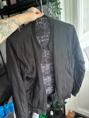 Svart quiltad bomberjacka - Stilren svart bomberjacka med quiltat mönster och ribbade muddar. Jackan har dragkedja framtill och en snygg, mönstrad insida. Perfekt för dig som gillar en clean look med lite edge. Jackan går även att vända på om du vill ha mönstrade sidan utåt. Båda sidor har fickor. Den mönstrade sidan är lite ful i färgen på ena sidan. Syns inte på avstånd men om man tittar nära. 