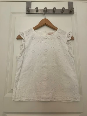 Broderad blus - Väldigt fin broderad blus med en liten volang vid ärmen med knappar baktill. Blusen är använd men i mycket fint skick.