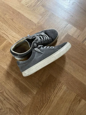 Grå mockasneakers med vit sula - Snygga grå sneakers i mocka med klassisk låg profil och vita gummisulor. Skorna har matchande grå skosnören och en stilren design som passar till det mesta. Perfekta för dig som gillar en clean och enkel look.