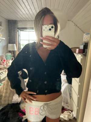 Svart kofta från H&M med knappar - Svart stickad kofta från H&M med v-ringning och knäppning framtill. Koftan har två små fickor framtill och långa ärmar. Perfekt att slänga på sig över en topp för en chill look.