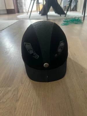 Svart ridhjälm med MIPS-system - Snygg svart ridhjälm med glittrig detalj och ventiler framtill. Använd 3 gånger och har aldrig ramlat av med den. Utrustad med MIPS-system för extra säkerhet.  Perfekt för dig som vill ha både stil och skydd i stallet.