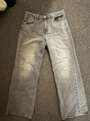Grå raka jeans med vintagekänsla - Säljer ett par grå jeans med rak passform och klassisk femficksdesign. Jeansen har en snygg tvättad look och är tillverkade i denim. Perfekta för dig som gillar en avslappnad och trendig stil.