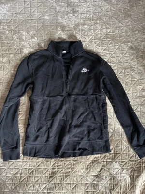 Svart Nike half-zip - Svart tjocktröja från Nike med halv dragkedja och hög krage. Klassisk Nike-logga i vitt.