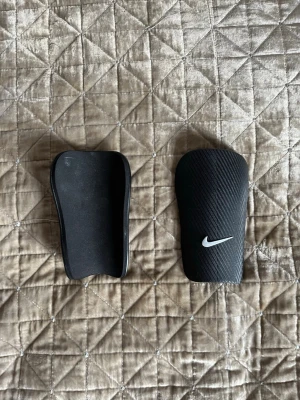 Svarta benskydd från Nike - Säljer ett par svarta benskydd från Nike med vit logga. Som ny skick.