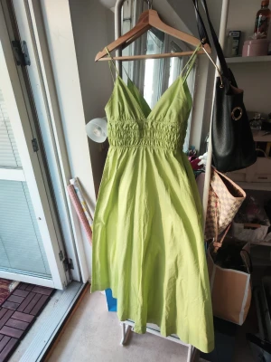 Ljusgrön långklänning från ZARA - Snygg ljusgrön långklänning från ZARA med smala axelband och v-ringad urringning. Klänningen har smockad överdel och ett luftigt fall i kjolen, perfekt för varma dagar. Tillverkad i ett lätt material som känns skönt mot huden.