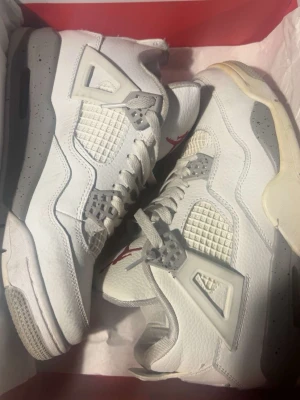 Air Jordan 4 White Oreo sneakers - Säljer ett par Air Jordan 4 White Oreo sneakers med vit ovandel i läder, meshdetaljer och gråa inslag med svarta prickar på mellansulan. Röd Jumpman-logga på plösen och klassiska plastdetaljer vid snörningen. Riktigt clean och ikonisk modell.