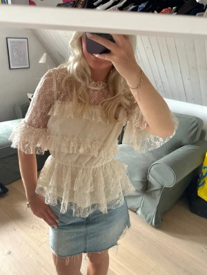 Vit spetsblus med volanger - Romantisk vit spetsblus med volanger och transparenta detaljer. Blusen har rund hals, markerad midja och trekvartsärmar med volangkant. Perfekt för dig som gillar en feminin och trendig stil.