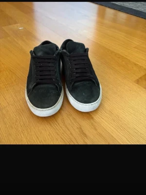 Svarta sneakers från Axel Arigato - Snygga svarta sneakers från Axel Arigato i mocka med svart snörning och vit sula. Klassisk låg modell med diskret logga på sidan. Perfekta till jeans eller streetwear-stil.