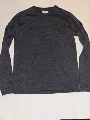 Grå stickad tröja från Lindbergh - Mysig grå stickad tröja från Lindbergh med relaxed fit. Tröjan har rund halsringning och långa ärmar, perfekt för lager-på-lager och enkel att matcha med olika outfits.