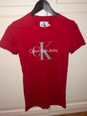 Calvin Klein Jeans t-shirt  - Två snygga t-shirts från Calvin Klein Jeans med klassiskt CK-logotryck på bröstet. Den ena är röd och den andra är ljusrosa, båda i mjuk bomull och med korta ärmar. Perfekt för dig som gillar stilrena och trendiga plagg. Knappts använt och är därmed i nyskick 