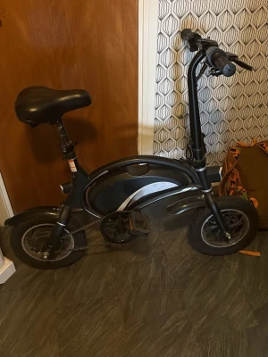 Svart elcykel med digital display - Säljer en kompakt svart elcykel med digital display på styret och robust ram i metall. Cykeln har små hjul, justerbar sadel och handtag med bromsar samt en on/off-knapp. Perfekt för kortare pendling och smidig att förvara inomhus. Bromsarna funkar inte och om du är intresserad kan jag säga vart vi kan möta upp inom Stockholm 