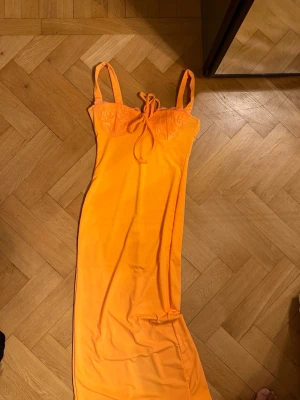 Långt orange nattlinne med spets - Säljer ett långt klänning  i stark orange färg med smala axelband och dekorativ spets upptill. Klänningen  har en slimmad passform och knytband vid bysten. Materialet är mjukt och följsamt, perfekt för att gå ut 