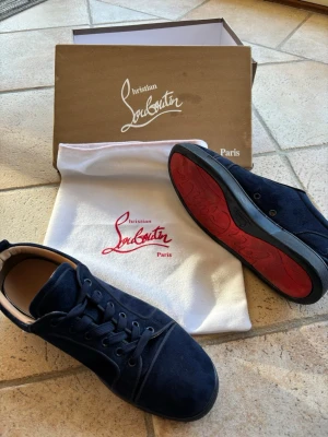 Blåa Christian Louboutin 42 - Snygga mörkblå sneakers från Christian Louboutin med klassisk röd sula och ovandel i mocka. Skorna har en låg profil och stilrena snörningar. Perfekt för dig som vill ha något exklusivt och trendigt i garderoben.