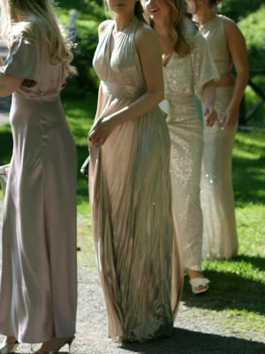 Lång glittrig champagnefärgad klänning - Säljer en elegant långklänning i glittrigt champagnefärgat tyg. Klänningen har djup v-ringning, markerad midja och öppen rygg. Klänningen knyts själv i nacken. Materialet är glansigt och tungt så det faller snyggt. Perfekt för bal!💕