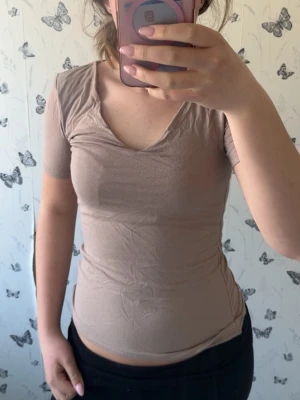 Beige v-ringad topp från New Yorker  - Säljer en beige topp från New Yorker i storlek XS. Toppen har korta ärmar, v-ringning och en slim passform som sitter snyggt på kroppen. Perfekt att matcha med både jeans och kjol för en enkel men stilren look💖Kolla in min profil för fler fina och trendiga plagg!