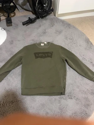 Olivgrön sweatshirt från Levi's - Säljer en olivgrön sweatshirt från Levi's med klassisk logga i svart på bröstet. Tröjan har rund halsringning och långa ärmar. Perfekt för en avslappnad och stilren look.