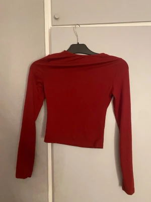 Mörkröd croppad långärmad topp - Snygg mörkröd croppad topp med långa ärmar och enkel design. Perfekt för att matcha med jeans eller kjol. Tunn och stretchig, passar dig som gillar stilrena plagg med lite edge.