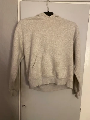 Ljusgrå hoodie med huva - Ljusgrå hoodie med klassisk huva och stor magficka framtill. Tröjan har ribbade muddar vid ärmslut och nederkant, och är tillverkad i mjukt material som känns skönt mot huden. Perfekt för dig som gillar en enkel och clean stil.