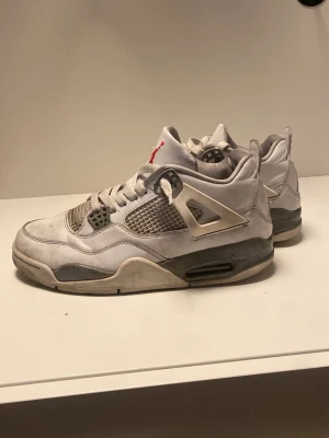 Air Jordan 4 oreo - Säljer ett par Air Jordan 4 oreo sneakers. Skorna är vita med grå och svarta detaljer, meshpaneler på sidorna och den klassiska Jumpman-loggan på hälen. Ovandelen är i läder och mesh, och sulan har synlig Air-enhet. Perfekt för dig som gillar ikoniska sneakers.