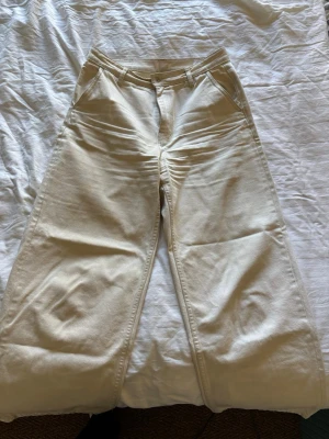Vida benvita jeans  - Säljer ett par snygga beige jeans med raka, vida ben och hög midja. Materialet är kraftigt denim i bomull och färgen är benvit/ljusbeige. Perfekta till en avslappnad stil.