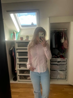 Ljusrosa skjorta med knappar - Säljer en ljusrosa skjorta med lång ärm och klassisk krage. Skjortan har knappar framtill och är figursydd för en snygg passform. Perfekt till jeans eller kjol för en clean och fräsch look. Sitter som Small/ XS