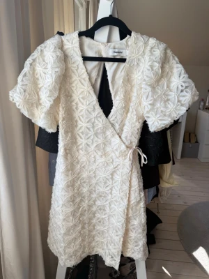 Vit omlottklänning från Kappahl - Superfin vit kortklänning från Kappahl med puffärmar och broderade blommor över hela tyget. Klänningen har omlottmodell med knyt i sidan och en öppen detalj i ryggen. Perfekt för student eller sommarens alla tillfällen! Klänningen är från Kappahl och i väldigt fint skick och endast använd en gång. Storlek xs.