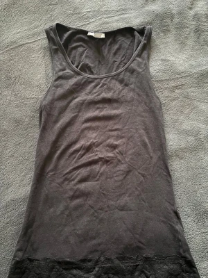 Svart linne med spetsdetalj ifrån New yorker - Snyggt svart linne med breda axelband och rund halsringning. Nederkanten är dekorerad med en elegant spets som ger en extra touch. Perfekt att matcha med jeans eller kjol. Materialet är mjukt och stretchigt, vilket gör linnet bekvämt att bära.