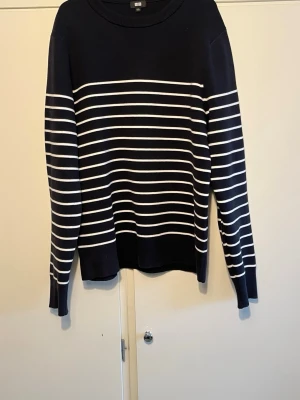 Marinblå randig tröja från Uniqlo - Snygg marinblå tröja från Uniqlo med vita horisontella ränder. Tröjan har rund halsringning och långa ärmar med ribbade muddar. Perfekt för en stilren look och tillverkad i mjukt material som känns skönt mot huden.