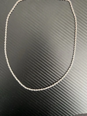 Flätat silverfärgat halsband - Säljer ett snyggt halsband med flätad kedja i silverfärgad metall. Halsbandet har en enkel och stilren design utan hängsmycken eller pärlor. Perfekt för dig som gillar minimalistiska accessoarer.