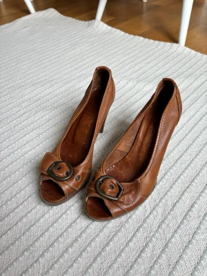 Bruna peep-toe pumps med spänne - Snygga bruna pumps i äkta läder med öppen tå och spänne framtill. 