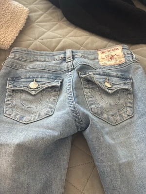 Blå low waist bootcut jeans true religion  - Säljer ett par blå low waist jeans med bootcut-modell från true religion Jeansen har klassiska fem fickor, bälteshällor och en snygg tvättad look. Passformen är tajt upptill och utsvängd nedtill. Köpta för 1300kr
