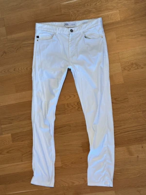 Vita slim fit jeans från Zara - Snygga vita slim fit jeans från Zara med klassisk femficksdesign och knappgylf. Jeansen har raka ben och är tillverkade i ett mjukt bomullsmaterial med lite stretch för extra komfort. Perfekta för en clean och fräsch look.