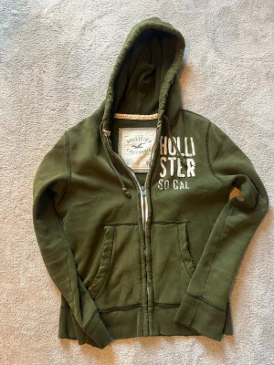 Grön hollister hoodie  - Säljer denna feta hollister hoodie. Den har en distressed look med små hål över tröjan. Tröjan är small men passar mig som är 185 skriv till mig vid frågor ! Priset kan sänkas vid snabb affär