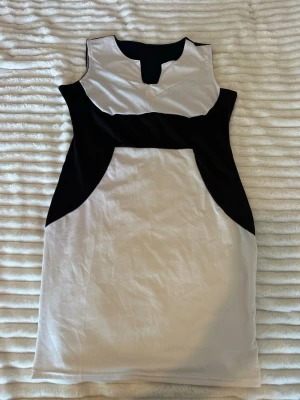 Svartvit ärmlös kortklänning - Snygg ärmlös klänning i svart och vitt med coola kontraster och figurnära passform. Klänningen har en unik design med svart panel upptill och i sidorna, samt vit bas. Perfekt för dig som gillar stilrena och moderna plagg.